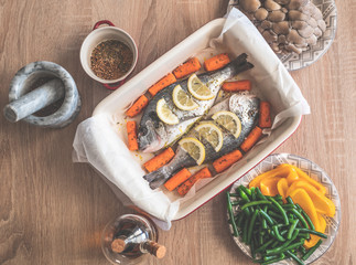 Raw dorado fish with spices lemon and vegetables, mushrooms cooking on baking tray.