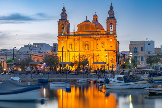 Valletta harbour with yachts and fishing boats, Msida Parish Church of Saint Joseph at sunset, Malta