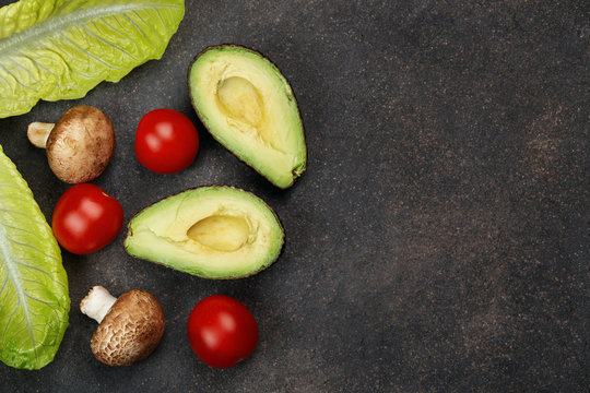 Avocado, cherry tomatoes, mushrooms, romaine lettuce on dark background.