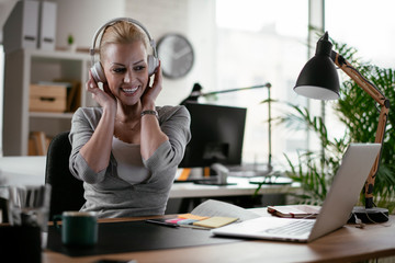 Portrait of businesswoman in office. Beautiful woman listening music at work.