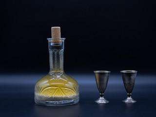 Vintage carafe with homemade vodka and the two metal glasses on the dark background. Alcoholic drink hrenovuha in transparent vintage bottle and pair of the iron shot.