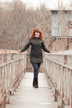 Young beautiful woman with red hair in a black jacket on a bridge in cloudy weather