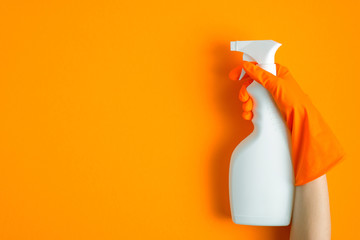 Female hand in glove holding cleaning spray over orange background. House cleaning service concept