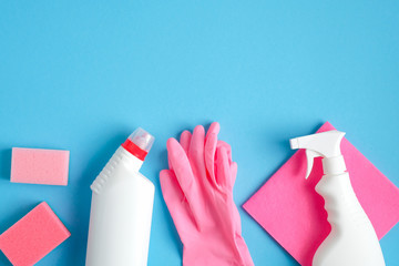 House cleaning service concept. Cleaning supplies on blue background. Top view pink sponge, rubber gloves, napkin and cleaner bottles
