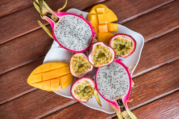 A mix of tropical fruits on a wooden table in a cafe. Passion fruit, mango and dragon fruit in a plate top view.