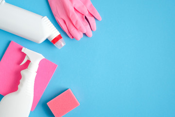 Cleaning supplies on blue background. Top view pink gloves, sponge, cleaner bottles. Cleaning...