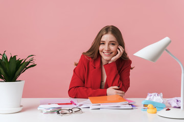 Woman sit at the table over pink wall background.