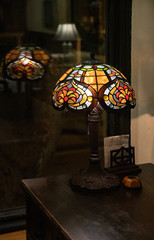 Old lamp. Antique table lamp with stained glass lampshade closeup on dark blurry background. Glowing mosaic lamp in shape of dome. Vintage table-lamp with ornate lamp shade made of colorful glass