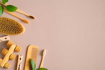 Eco-friendly bath accessories on brown background. Flat lay bamboo toothbrushes, hair comb, bath peeling brush, luffa sponge, massage tool and green leaves. Beauty and SPA treatment concept