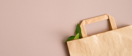 Recycled paper shopping bag with green leaves on brown background. Zero waste, plastic free...