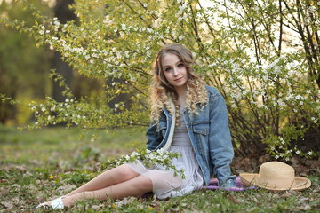 beautiful blonde in a blue denim jacket in a spring garden where trees bloom