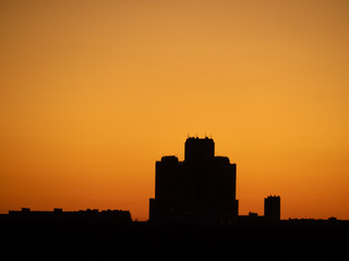 Fototapeta premium Skyscraper tower silhouette over dark forest on sunset and clear orange tone sky as background. Sunny weather (Moscow city, Russia)