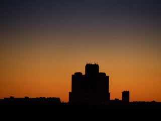 Fototapeta premium Skyscraper tower silhouette over dark forest on sunset and clear sky as background. Sunny weather (Moscow city, Russia)