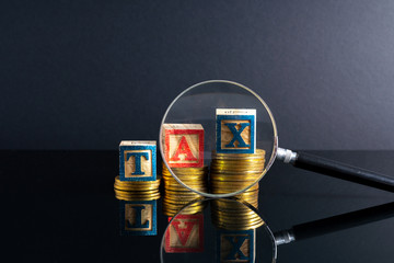 Magnifier glass and coins stacking and tax letter cube with low light view.