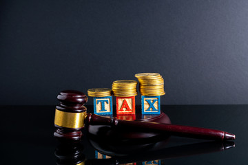 Gavel hammer and stacking coins and tax letter cube with low light view.