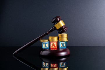 Gavel hammer and stacking coins and tax letter cube with low light view.