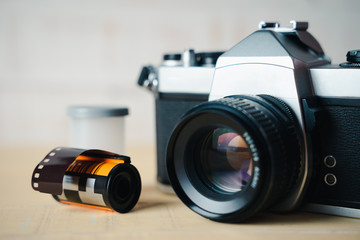 Old SLR film camera and a roll of film on wooden background.