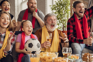 Excited, happy big family watching football, soccer match on the couch at home. Fans emotional...