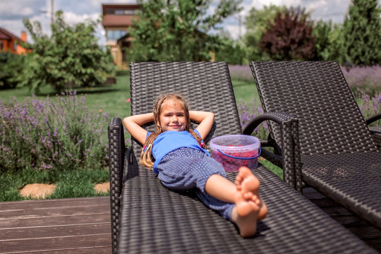 A cute little girl relaxing on the chaise longue at green garden outside, home feeling