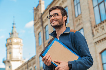 Young caucasian male student with books outside near campus