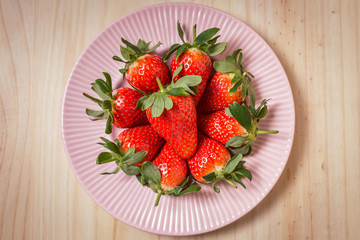 Strawberries in a pink plate on wooden table