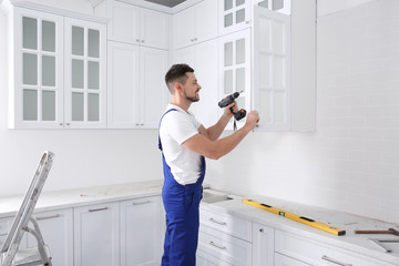 Fototapeta na wymiar Worker installing handle on cabinet door with screw gun in kitchen