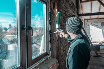 the builder fixes window with polyurethane foam - obrazy, fototapety, plakaty