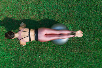 Sporty young woman doing stretching exercise with a ball in a dress field, balance posture. Beautiful athletic girl practicing yoga or pilates.