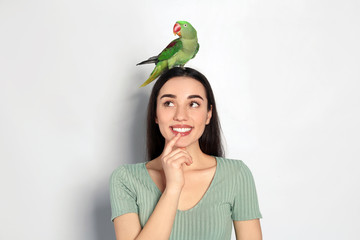 Young woman with Alexandrine parakeet on light background. Cute pet