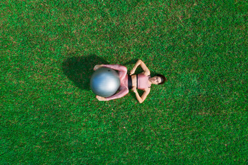Sporty young woman doing stretching exercise with a ball in a dress field, balance posture. Beautiful athletic girl practicing yoga or pilates.