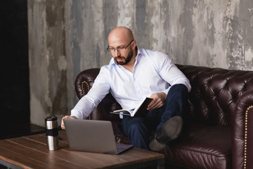 Fototapeta premium Thoughtful adult man working at a computer in the office. A stylish man with glasses does business with the help of modern technologies. Work online. Business portrait
