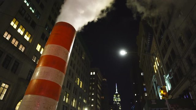 Steam rises and drifts among the rows of buildings along the Fifth Avenue at front of Empire State Building in the night at New York City NY USA during the Christmas Holidays seasons on Dec. 2018.