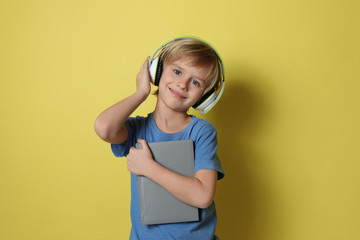 Cute little boy with headphones listening to audiobook on yellow background