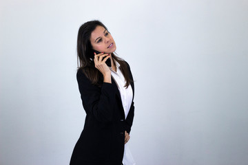 Portrait of attractive caucasian bussiness woman talking on mobile phone, isolated on gray background studio shot, white shirt and black jacket, dark air. Place for your text in copy space.