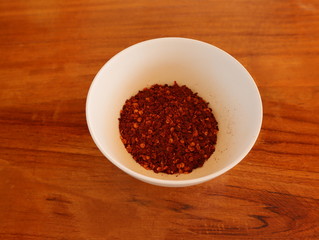 Red chilli powder on white cup with wooden table. 