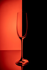 Empty champagne glass with reflection, on red and black gradient background. Club life concept.