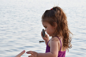 a little cute, very cute girl stands near the evening sea and looks at the water. Pensive, serious....