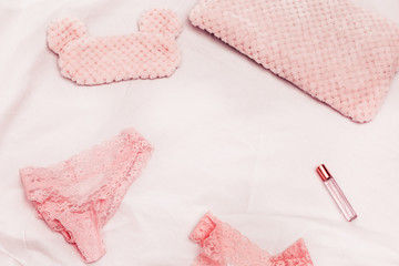 Set of lace underwear, sleep mask, perfume on white cotton sheet. Accessories for woman. Romance lifestyle and pink dreams. Top view and copy spsce.