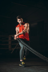 Training time in the cross fitness class good looking guy with a muscle body doing exercises with ropes make a hard and concentrated face