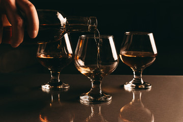 three glasses of cognac in one of which pour cognac from a bottle on a dark background