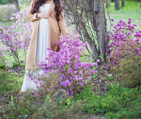 Obraz na płótnie Canvas Pregnant woman in white dress and beige coat near blossom tree