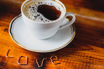 white cup of coffee on wooden table with word love on it 