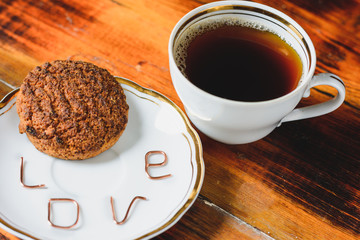 white cup with coffee and oatmeal cookies on a plate the inscription love from letters on a wooden table