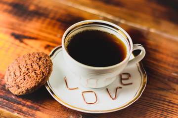 white cup with coffee on a plate of copper letters the inscription love with oatmeal cookies