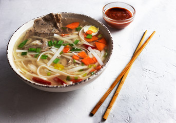 Pho bo soup, Asian cuisine, delicious soup on a gray background with spicy sauce.