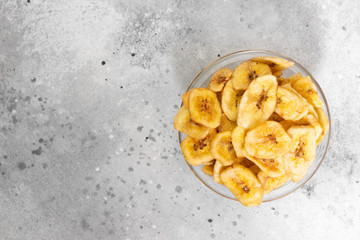 Dried bananas in a glass bowl on a gray kitchen table. Banana chips. Vegetarian snack for proper nutrition. Top view with space for text	