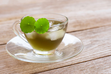 Cup glass of Gotu kola juice ice tea with leaf on wood background .