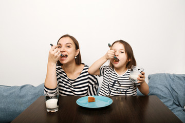 Mother and little kid daughter eating cake together with milk in the morning in light kitchen