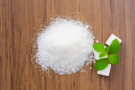 White sugar with stevia leaf on wood background. Top view.