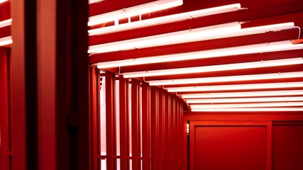 Selective focus and blurred foreground of red steel curve wall and door with many fluorescent lights on the vaulted ceiling inside of corridor